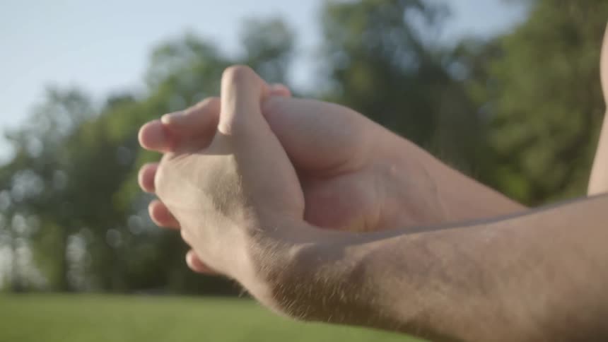 A man doing wrist stretches outdoors in a field during the day