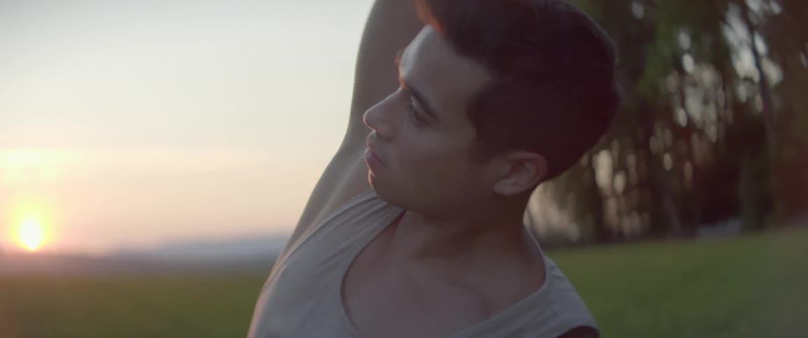A man in a tank top does yoga in a grassy field at sunset