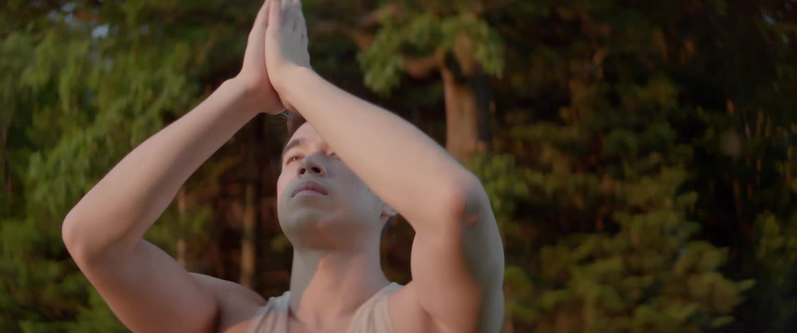 A man raises his arms and brings his hands together as he stretches and meditates outside