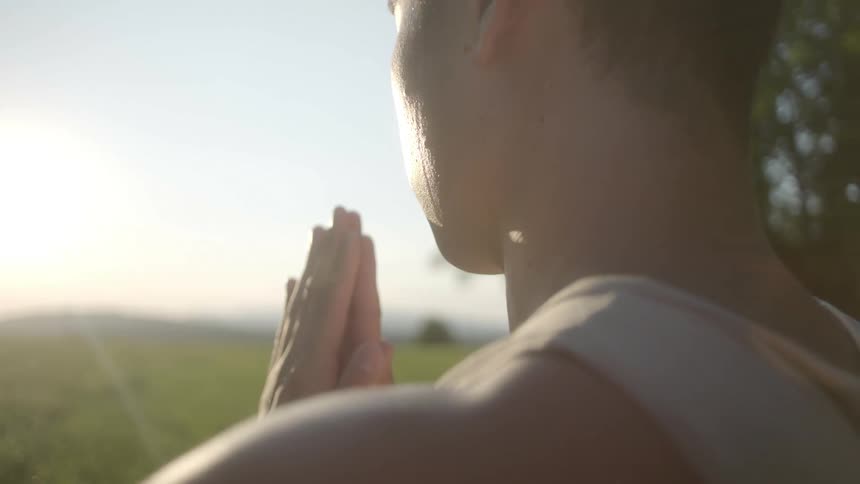 An asian man in a tanktop mediates in a field of grass on a sunny day