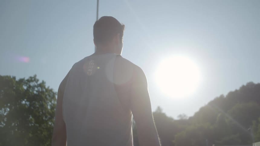 A barefoot man carrying a yoga mat walks on a bridge path in the park