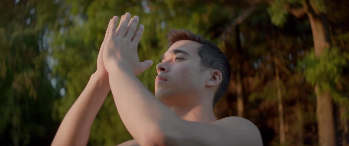 A man performing yoga movements with his arms while outdoors near a woodland