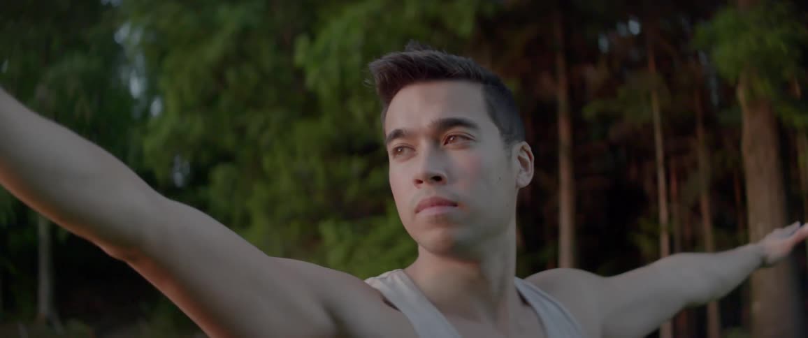A man in a tank top does yoga outside near trees