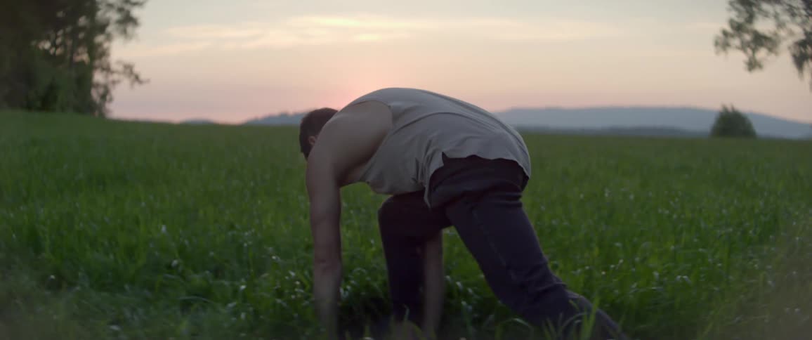 A man stretching on a grassy field with the sky and the sun in the background
