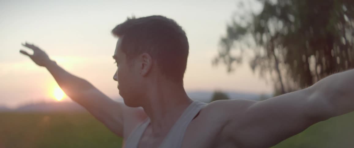 A man in a tank top does yoga in a grassy field at sunset