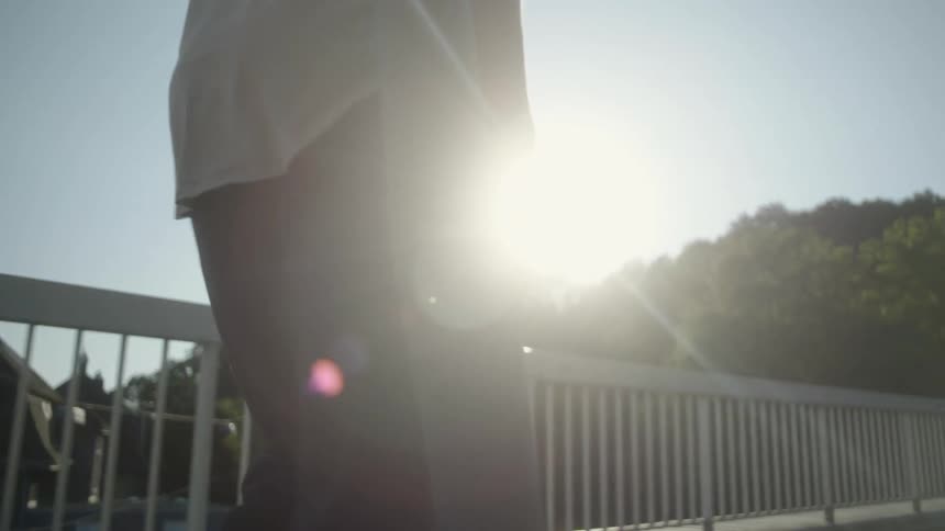 A person holding a mat walking on a bridge with houses trees and the sky in the background