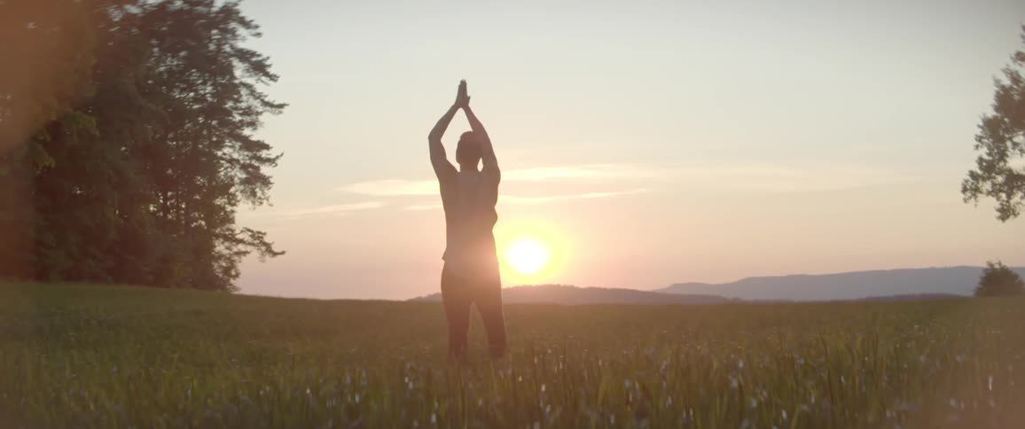 A man stretching on a grassy field with the sky and the sun in the background