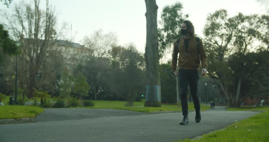 A teenager walking through a public park pulls out his phone and looks at it