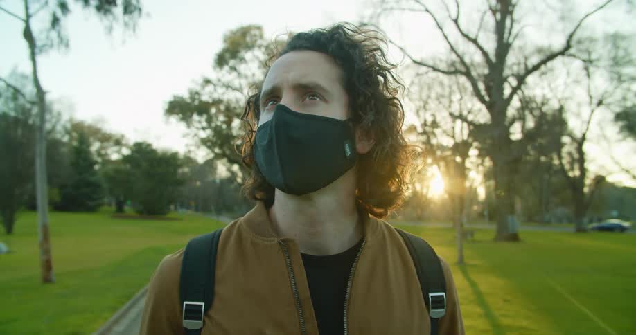 A man stands on a sidewalk in a public park and looks around as traffic passes by