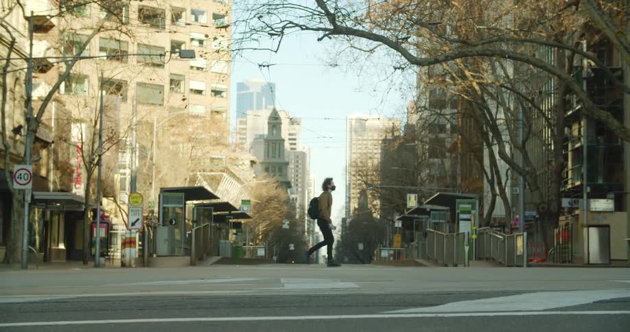 A man wearing a mask walks across the empty street of a large city
