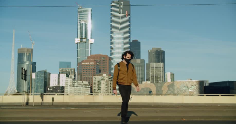 Man wearing face mask walks along empty highway with downtown skyscrapers inbackground