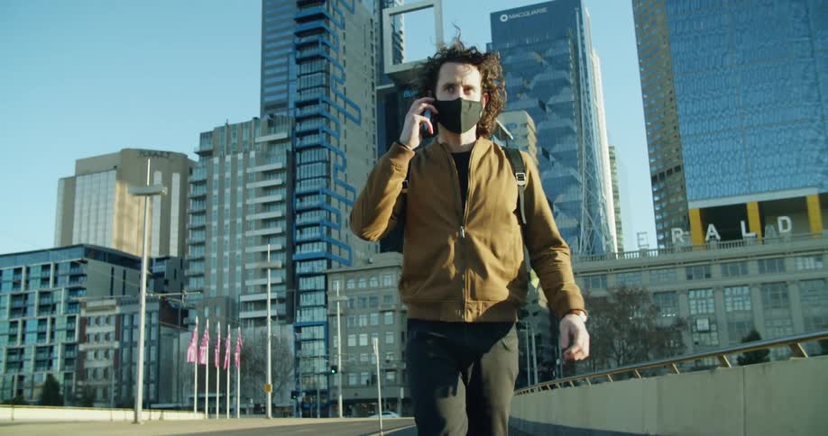 A man walks across a bridge in a metropolis while raising a smartphone to his ear