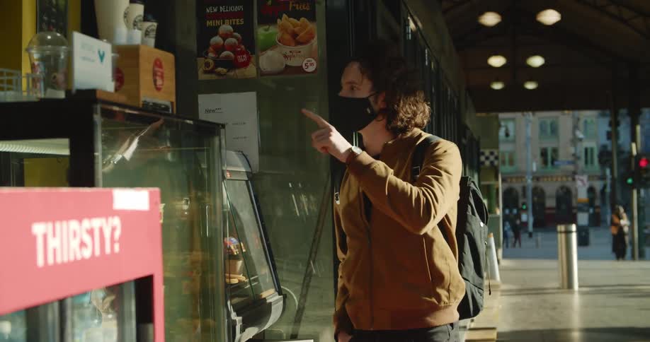 Man wearing a face mask orders at food storefront under covered sidewalk