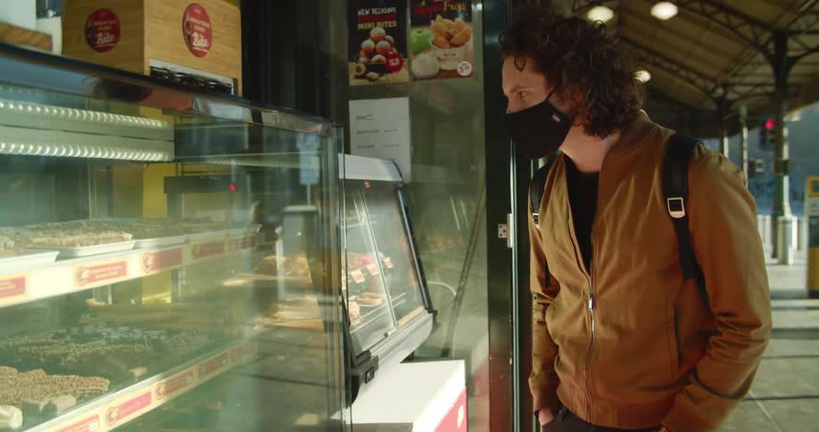 A teenager stops at a market on a city street and looks at the food in the case