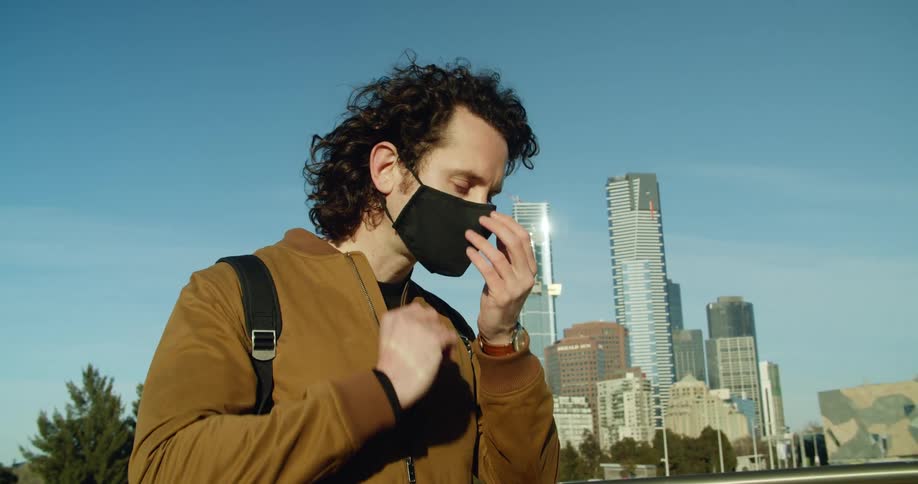 A man puts on a black face mask as he stands in front of a city skyline