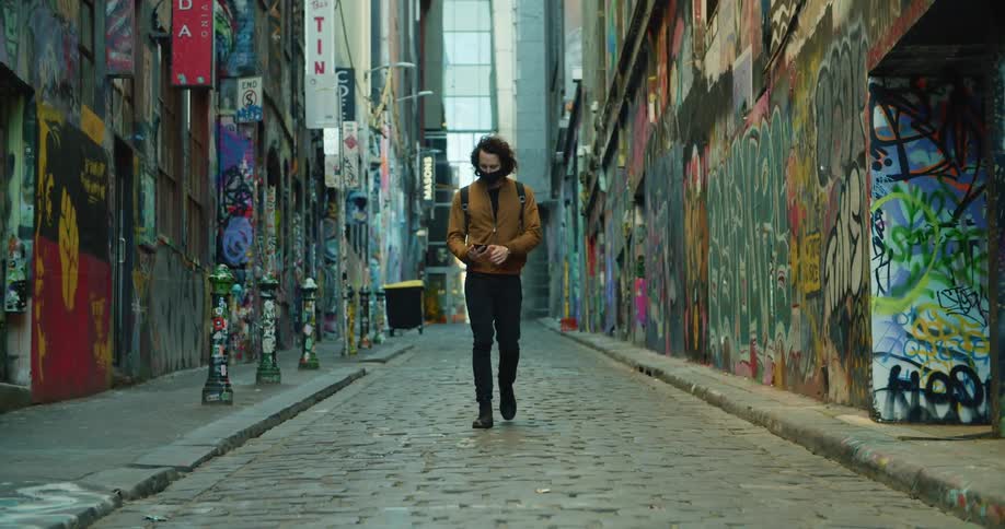 A man walks down a cobblestone alley lined with graffiti tagged buildings