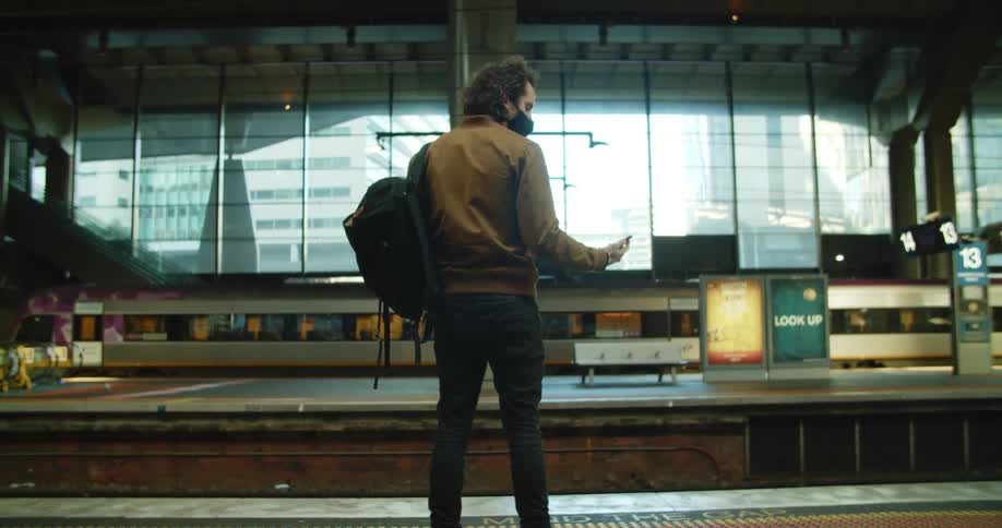 A man standing on a platform waiting for a train checks his phone