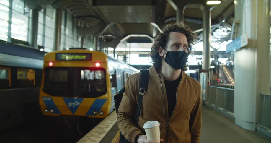 A man carrying a cup of coffee walks on a platform as a train leaves the station