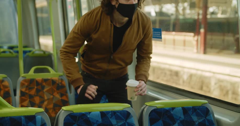 A man takes off his backpack and sits down on a seat in an empty train car