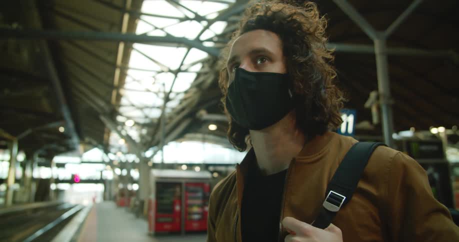 Male waiting alone on subway platform for the train while looking at his cellphone then looks up and at his watch to check the time
