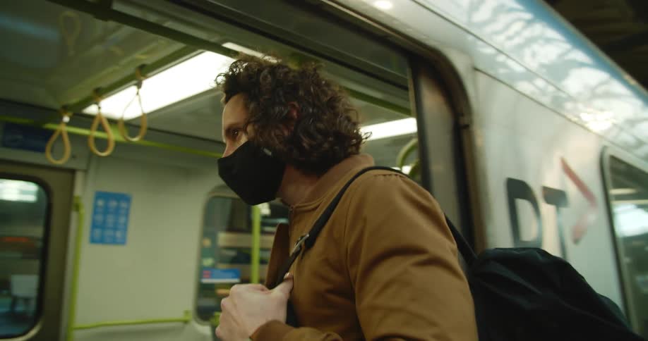 A man wearing a mask and holding a smart phone enters a subway