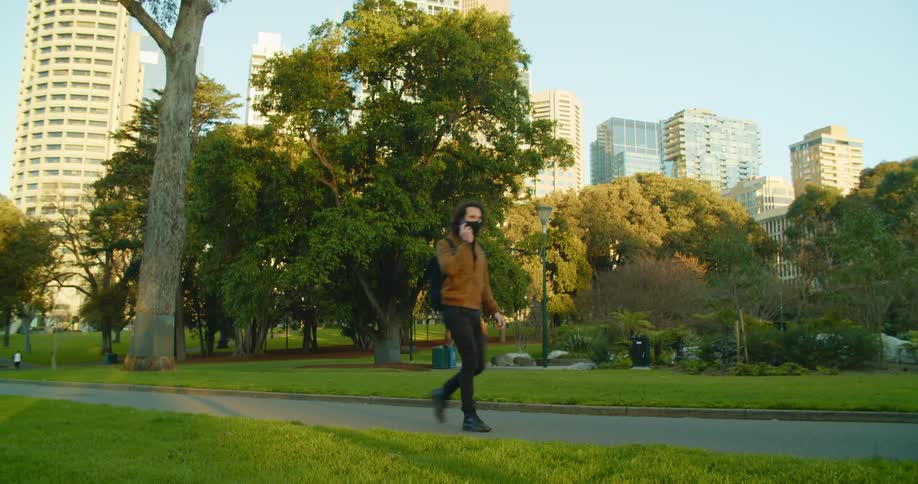 Man walks through empty park near downtown talking on mobile phone