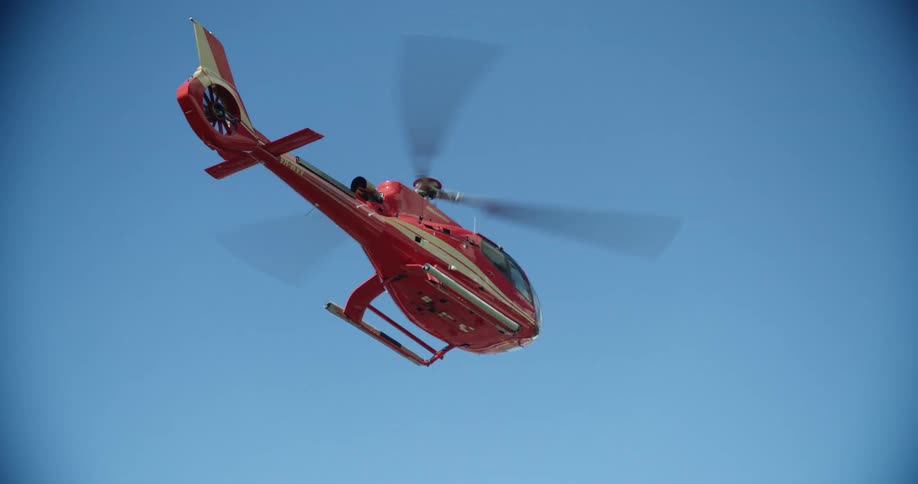 A red helicopter flying in a bright blue sky