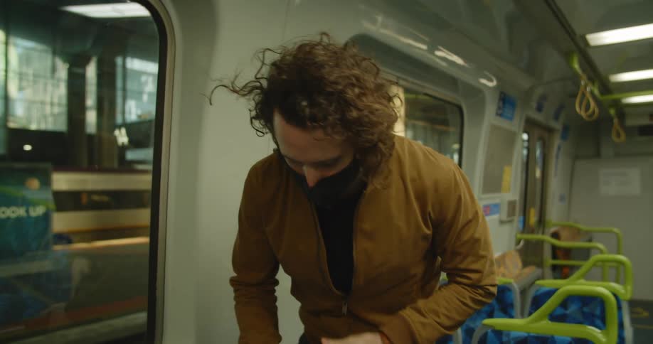 Man wearing face mask sets backpack down and takes seat on empty public transportation