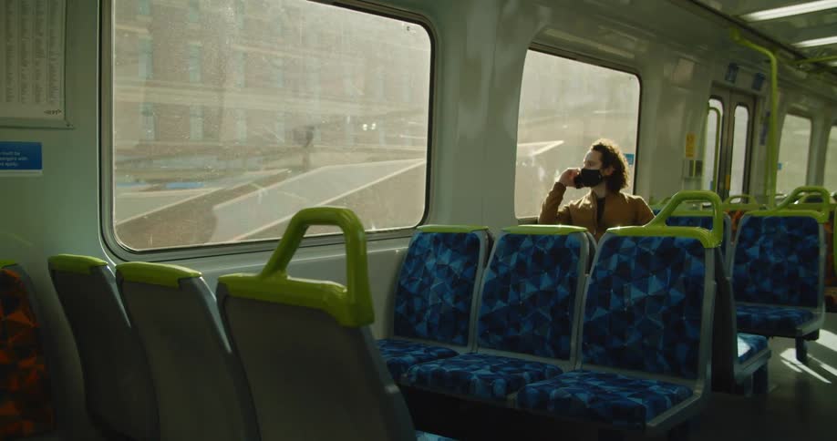 A man raises a smartphone to his ear while sitting on a train traveling through a city