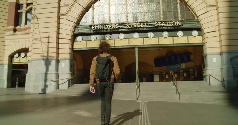 A man wearing a black medical mask walks towards the entrance of a train station in a city during the day
