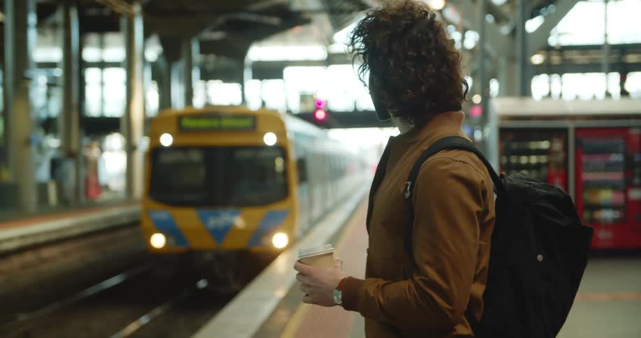 A teenager holding a coffee waits for a subway at a station