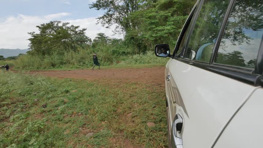 A vehicle driving towards african tribesmen as they walk along a dirt road
