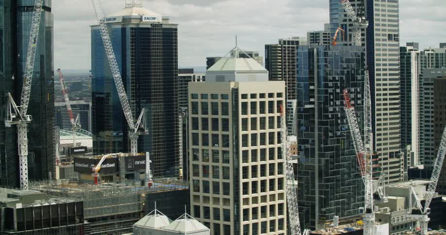 Construction cranes dot roofs in tower block under cloudy sky