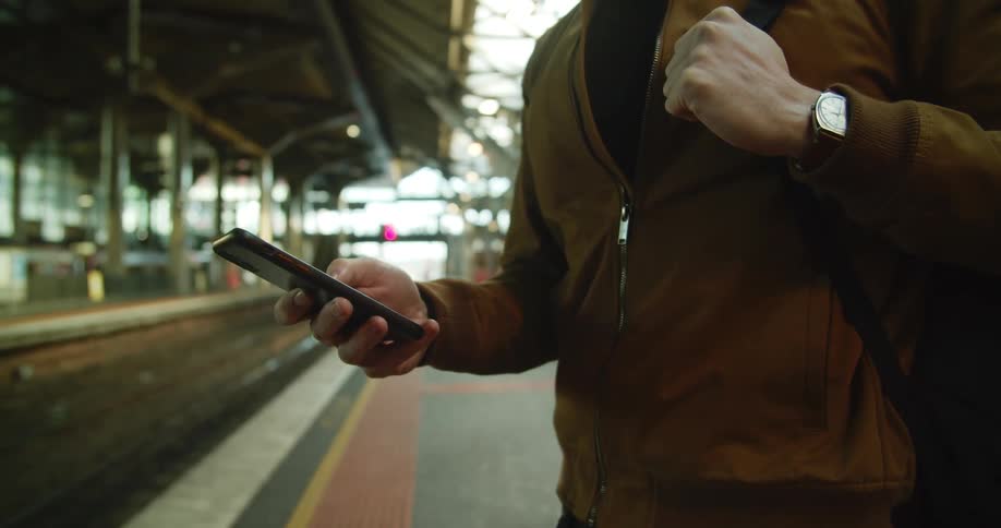 A man uses his cell phone while waiting next to tracks at a train station