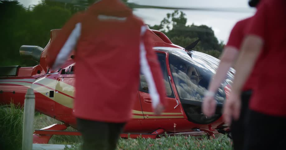 Three men walking toward a helicopter with trees and the sky in the background