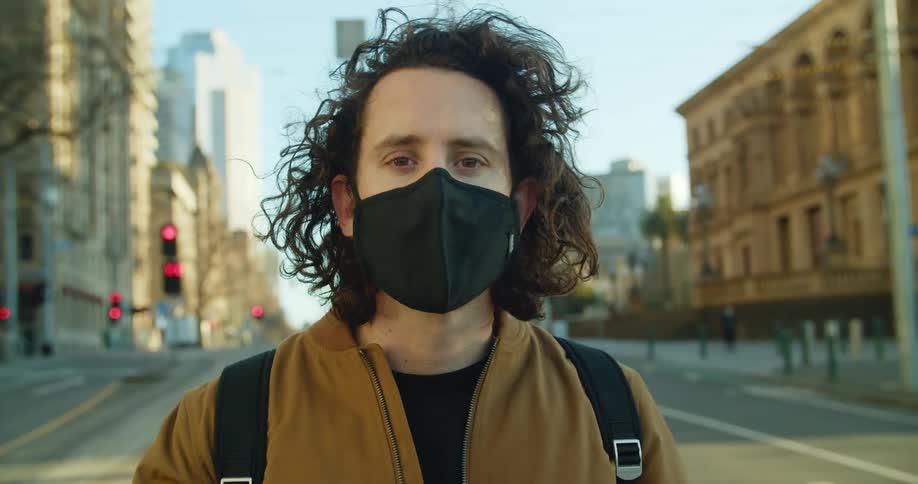 A man stands on an empty city street and puts on a mask