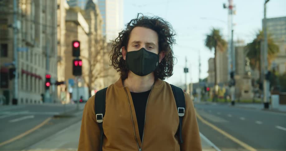 A man wearing a mask stands in the middle of an empty city street