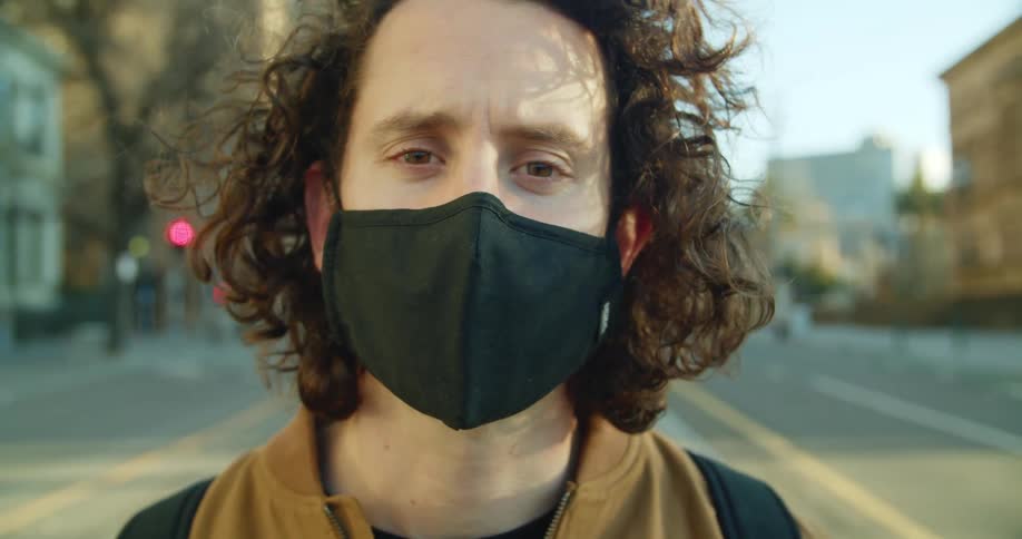 A teenager standing on a city street wearing a mask