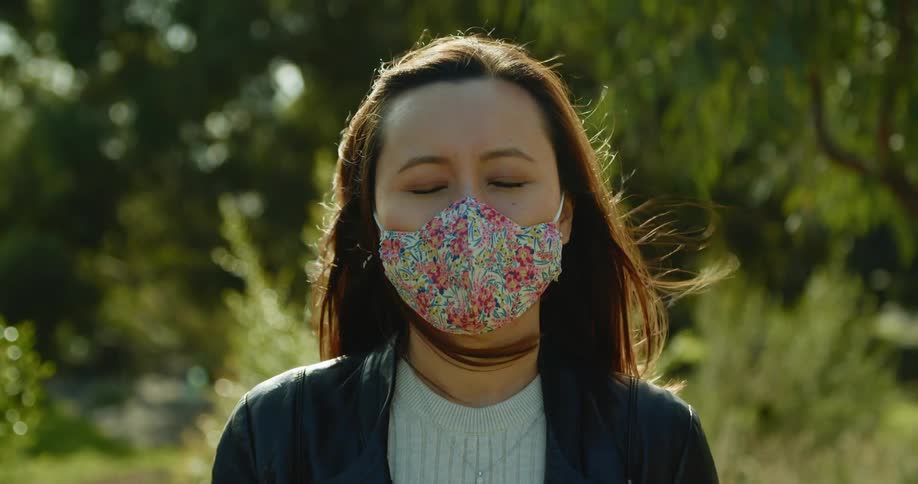 A woman is standing outdoors while wearing a face mask