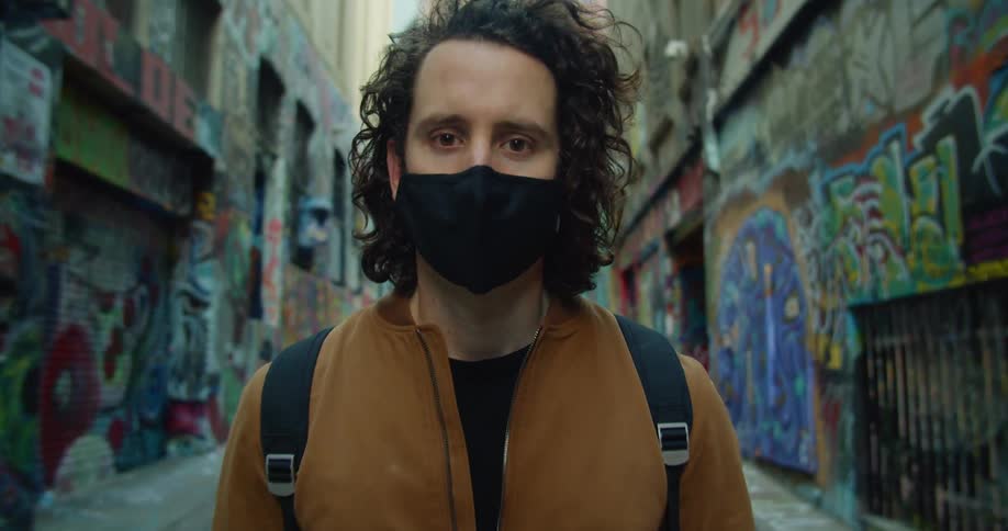 A man stands in a street with buildings covered in graffiti on both sides