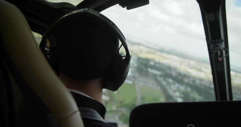 The head of a pilot wearing a headset flying a helicopter