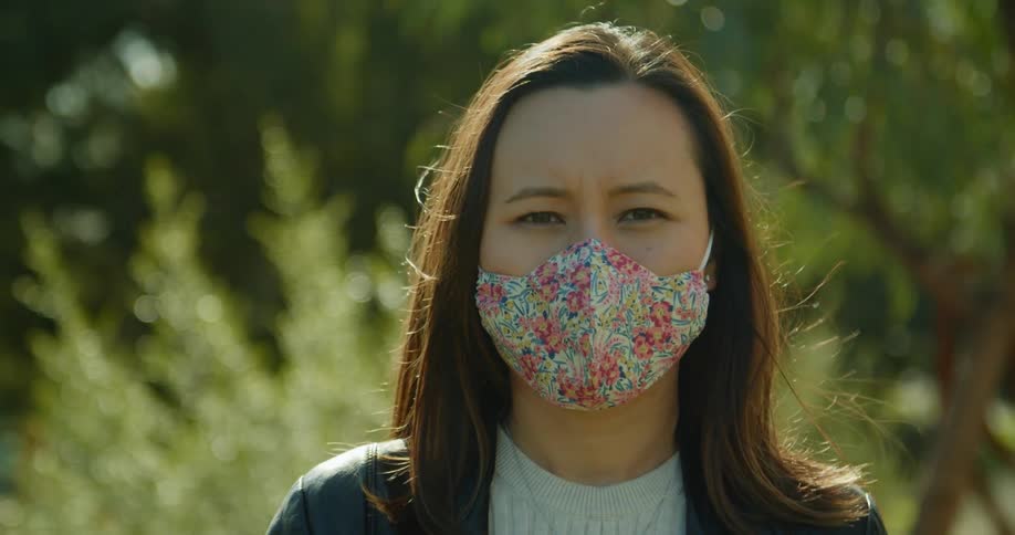Woman standing outdoors wearing floral face mask turns to camera