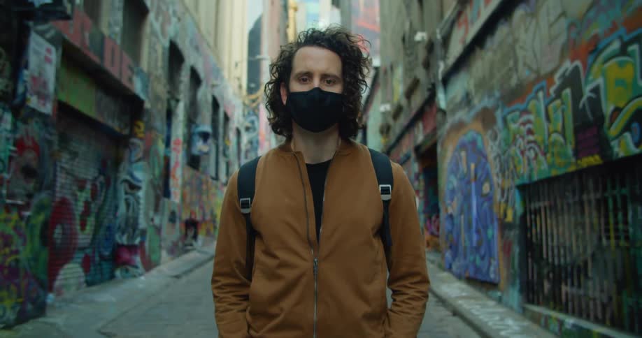 A man wearing a medical mask stands in a city alley covered in graffiti