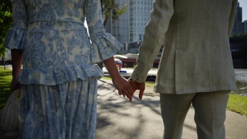 A man and woman walk a long a path next to the water while holding hands