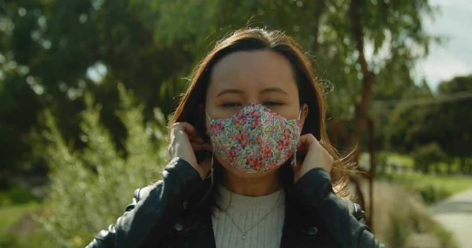 Woman puts on face mask standing in park near paved path