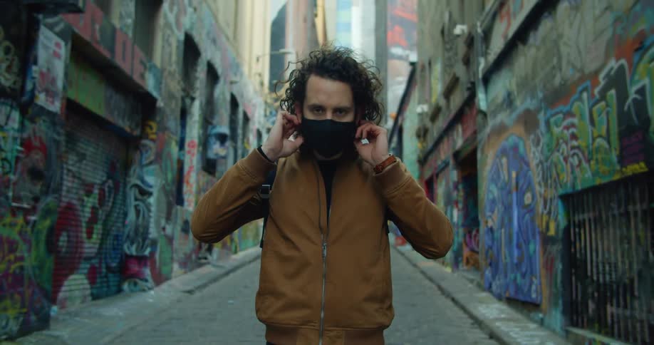 Man standing in graffiti covered alley near downtown puts on face mask