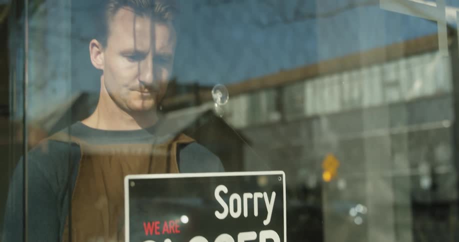 A business owner flips the sign in his glass doorway from open to closed