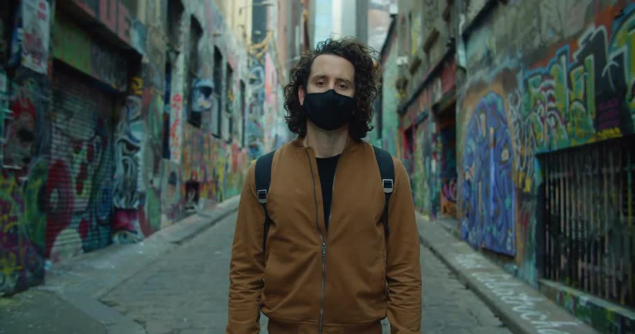 A man with a mask and backpack standing in an alley with graffiti on the walls