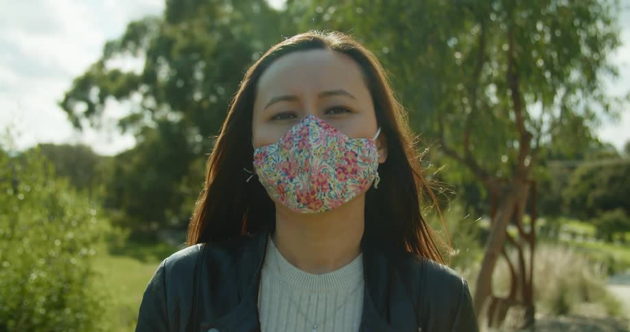 A woman wears a floral face mask as she stands near trees in a park