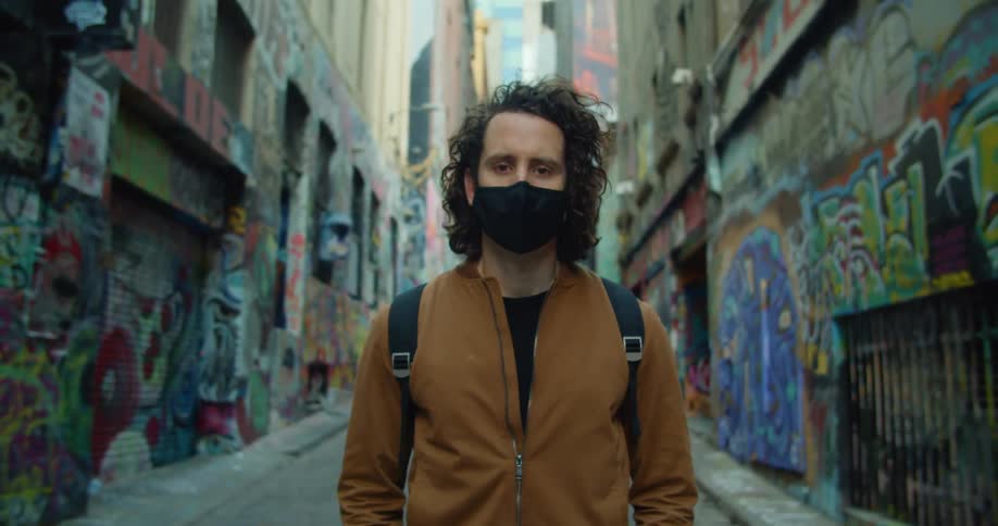 A man in a mask is standing in the empty alley